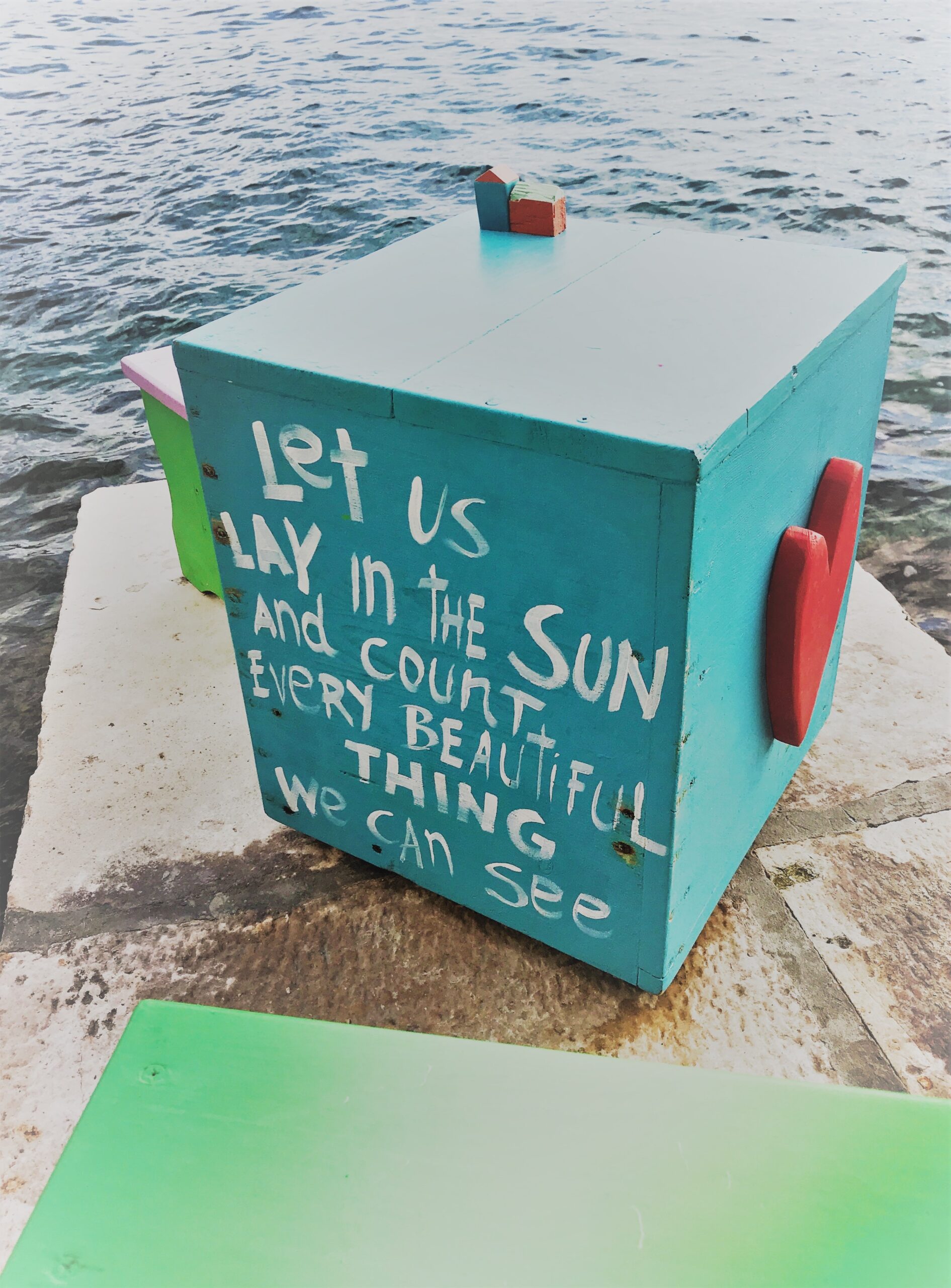 türkise Box am Meer mit der Aufschrift: let us lay in the sund